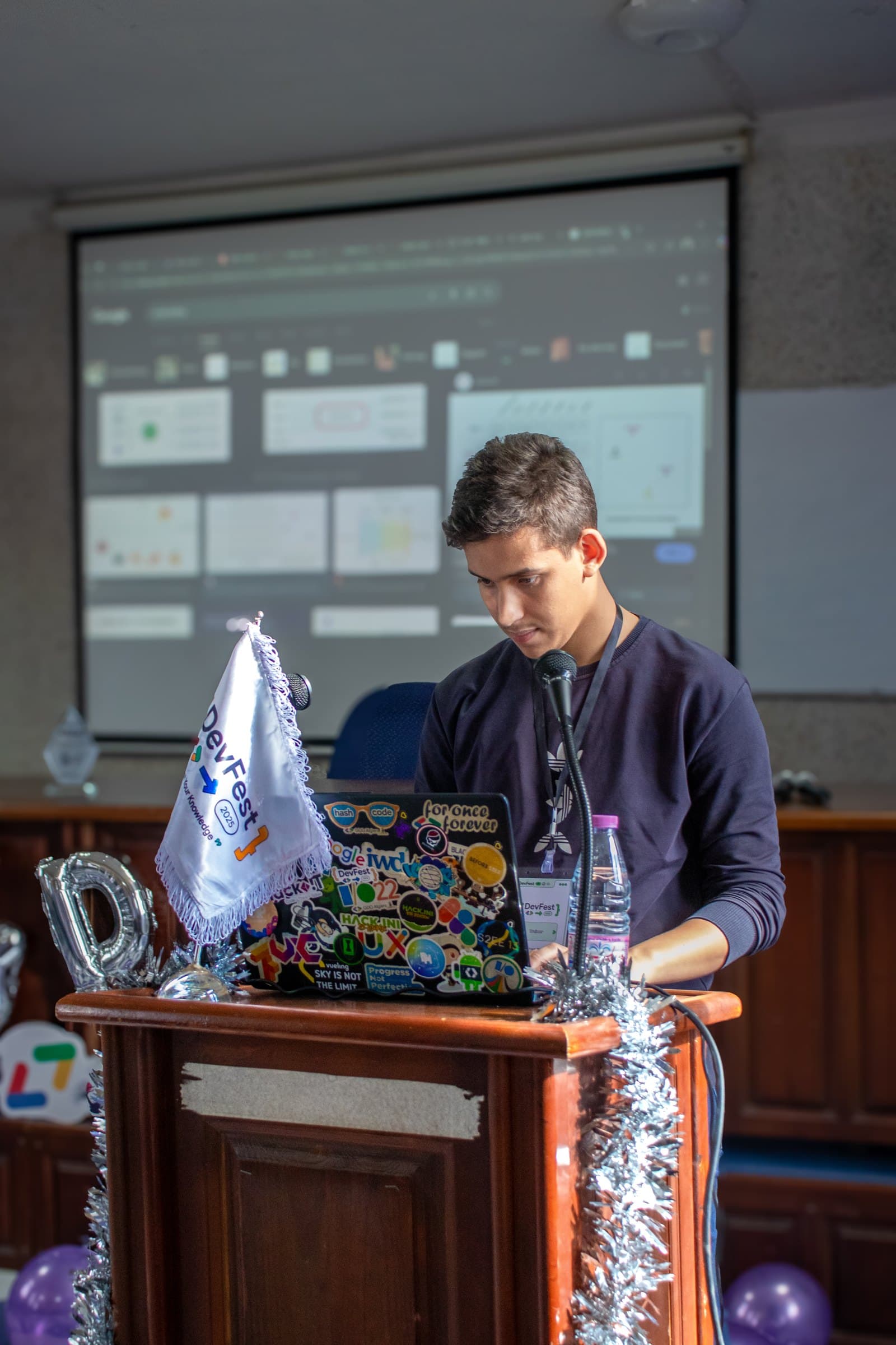 Chamel Nadir Bouacha at the lectern presenting RAG in the Era of LLMs at DevFest Algiers 2025, his slides on the screen behind him